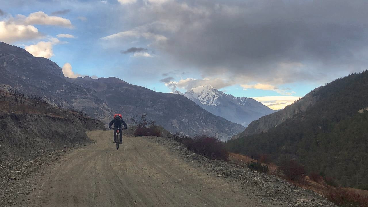 Bishal Shrestha, Yachu's founder, riding a mountain bike through Manang, above 3,500 m, with a snow peak ahead