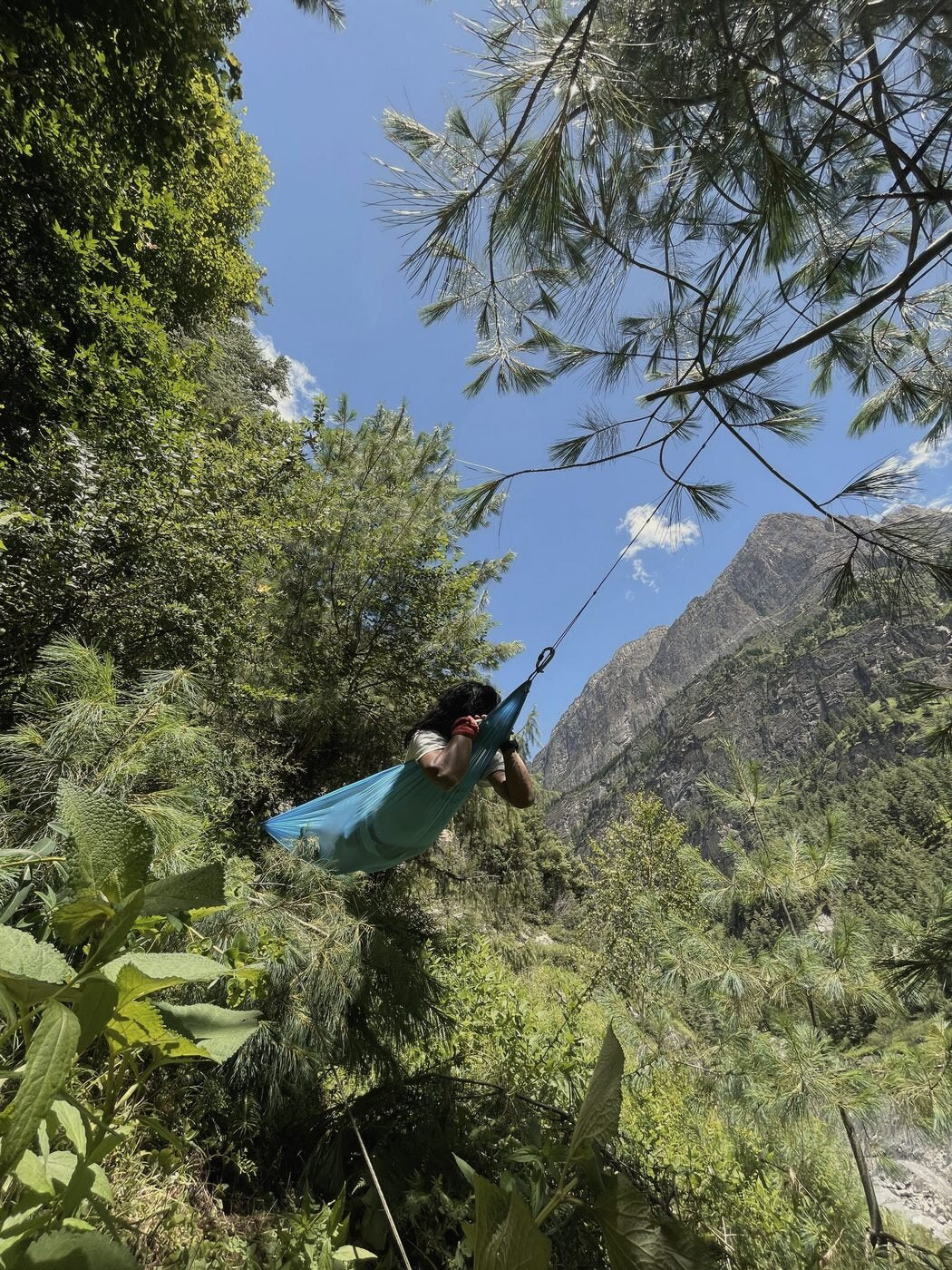 Someone sitting in the blue Airlite Hammock under pine trees in Manang